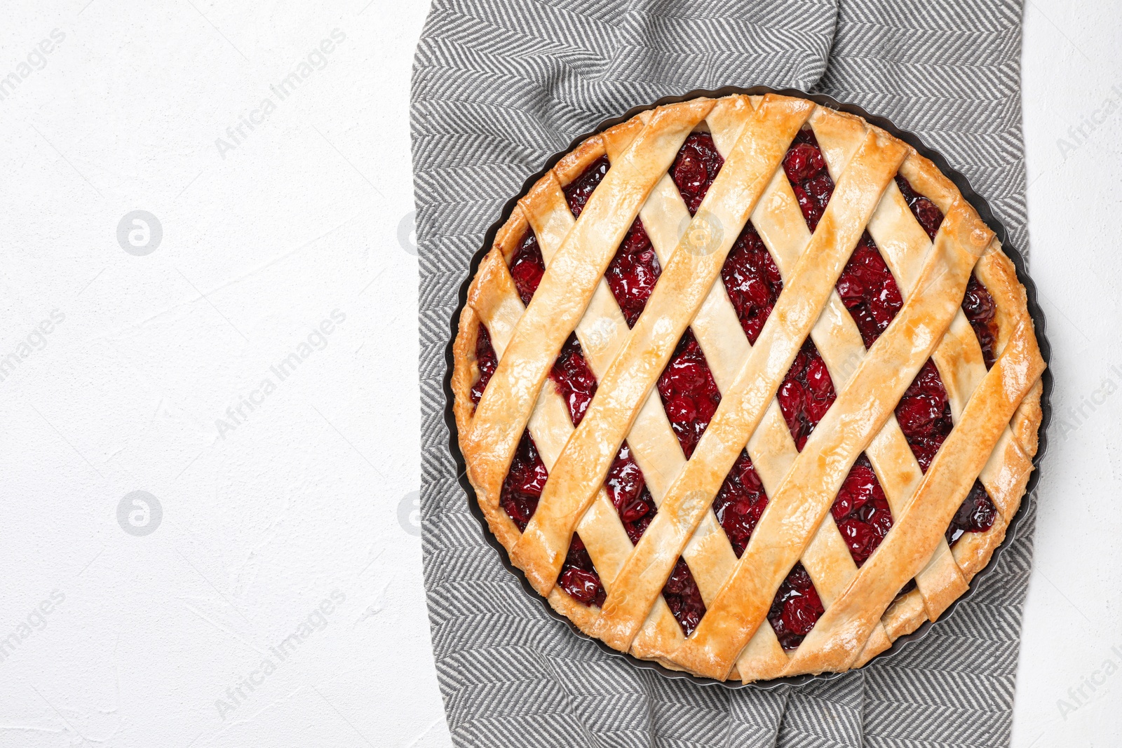 Photo of Delicious fresh cherry pie and grey towel on white table, top view. Space for text