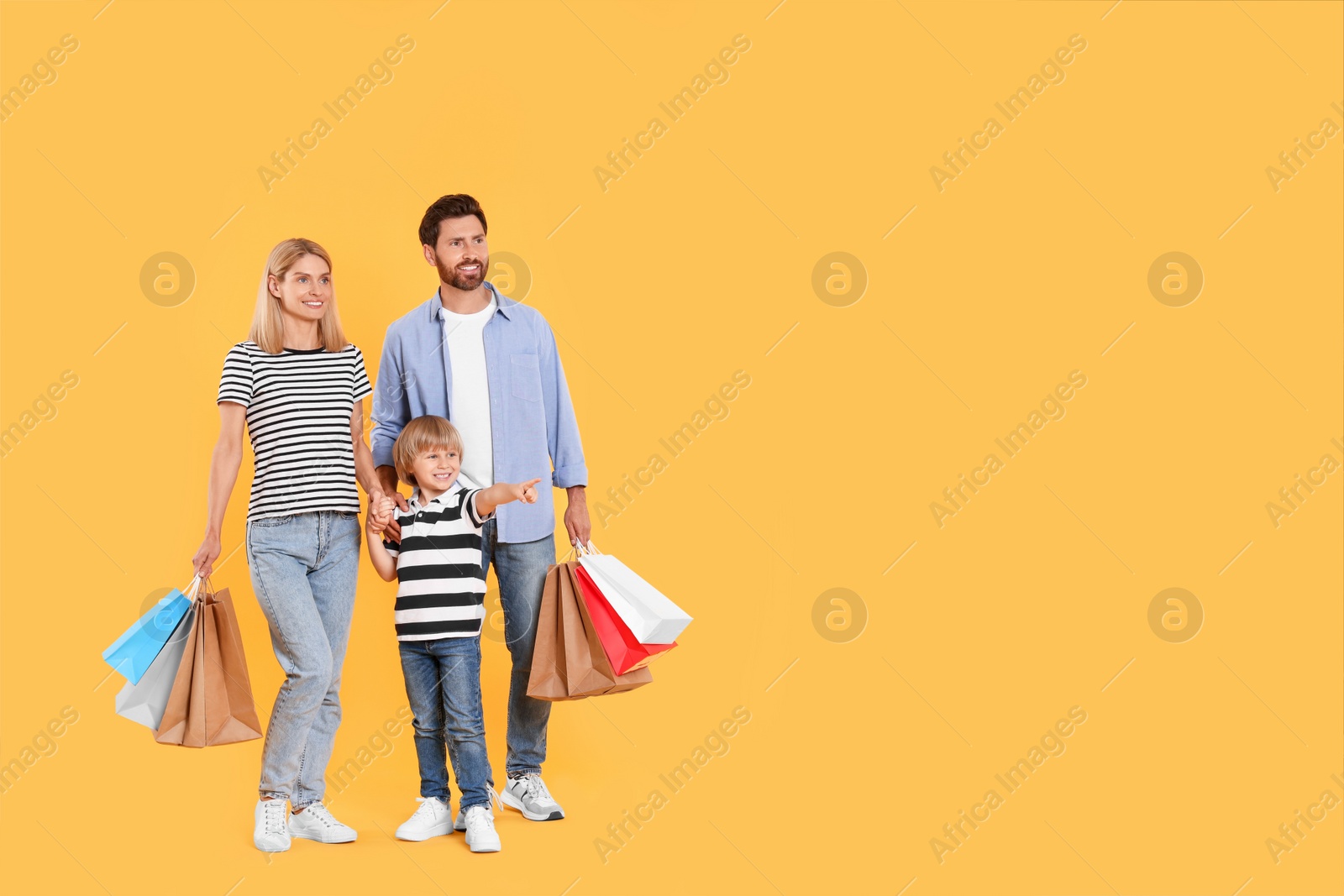 Photo of Family shopping. Happy parents and son with paper bags on orange background. Space for text