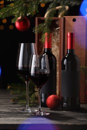 Photo of Bottles of wine, glasses, wooden boxes, fir twigs and red Christmas balls on table