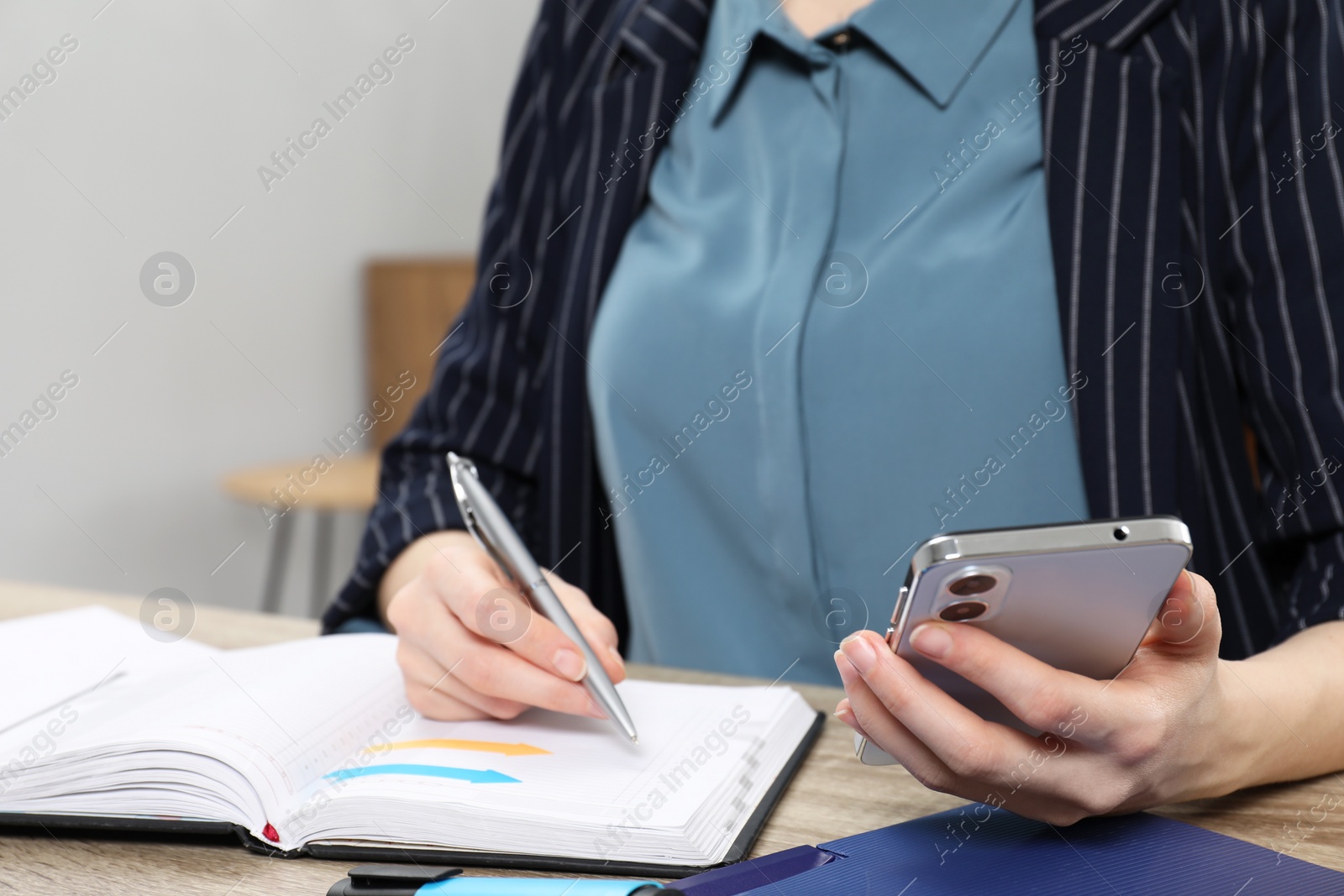 Photo of Woman taking notes while using smartphone at wooden table indoors, closeup. Space for text