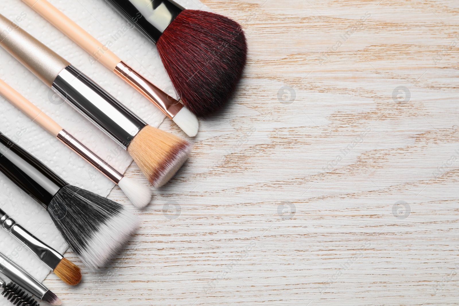 Photo of Clean makeup brushes with napkin on wooden table, flat lay. Space for text