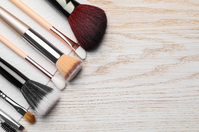 Clean makeup brushes with napkin on wooden table, flat lay. Space for text