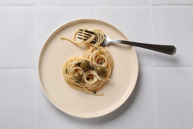 Photo of Heart made of tasty spaghetti, fork, olives and cheese on white tiled table, top view