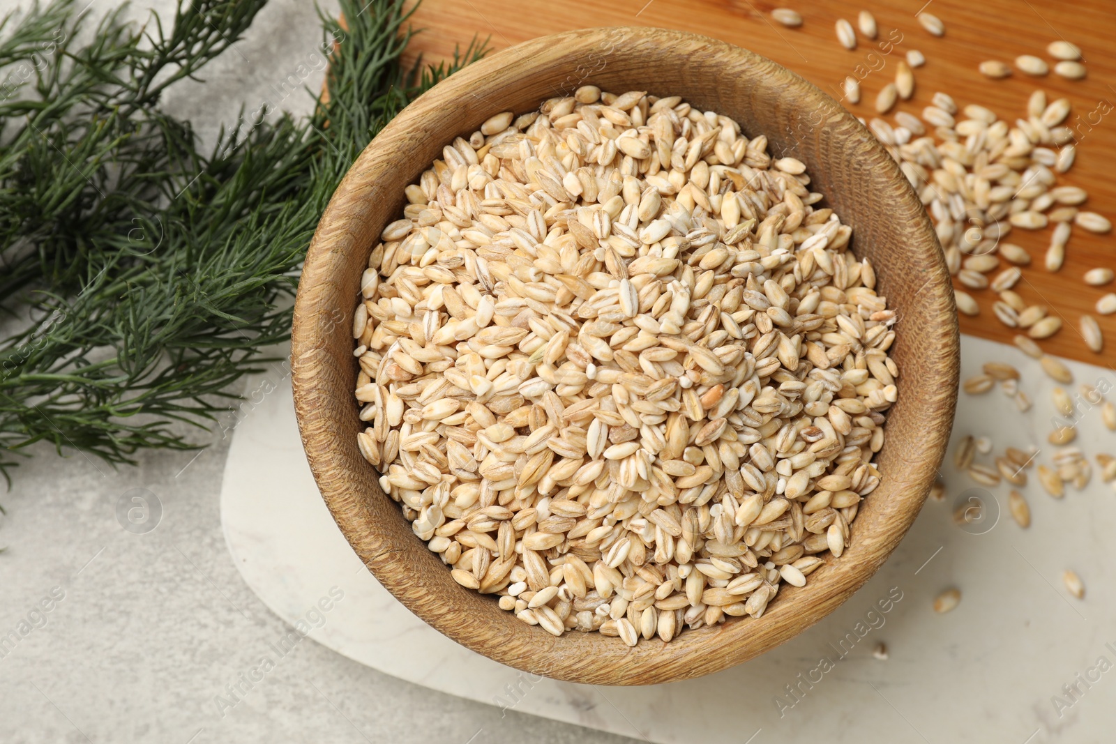 Photo of Dry pearl barley in bowl and dill on table, top view