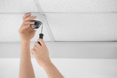 Photo of Technician installing CCTV camera on ceiling indoors, closeup