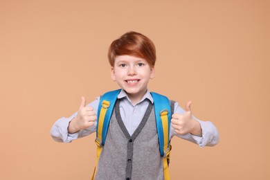 Photo of Smiling schoolboy showing thumbs up on beige background