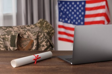 Laptop and diploma on wooden table near flag of United States indoors. Military education