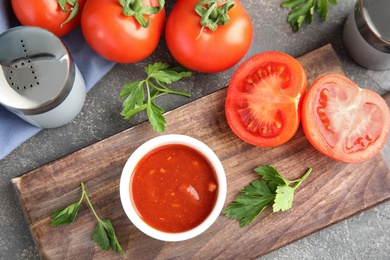 Photo of Flat lay composition with bowl of sauce and tomatoes on grey table