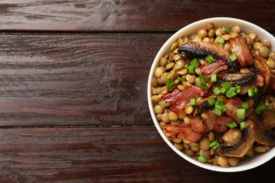 Photo of Delicious lentils with mushrooms, bacon and green onion in bowl on wooden table, top view. Space for text