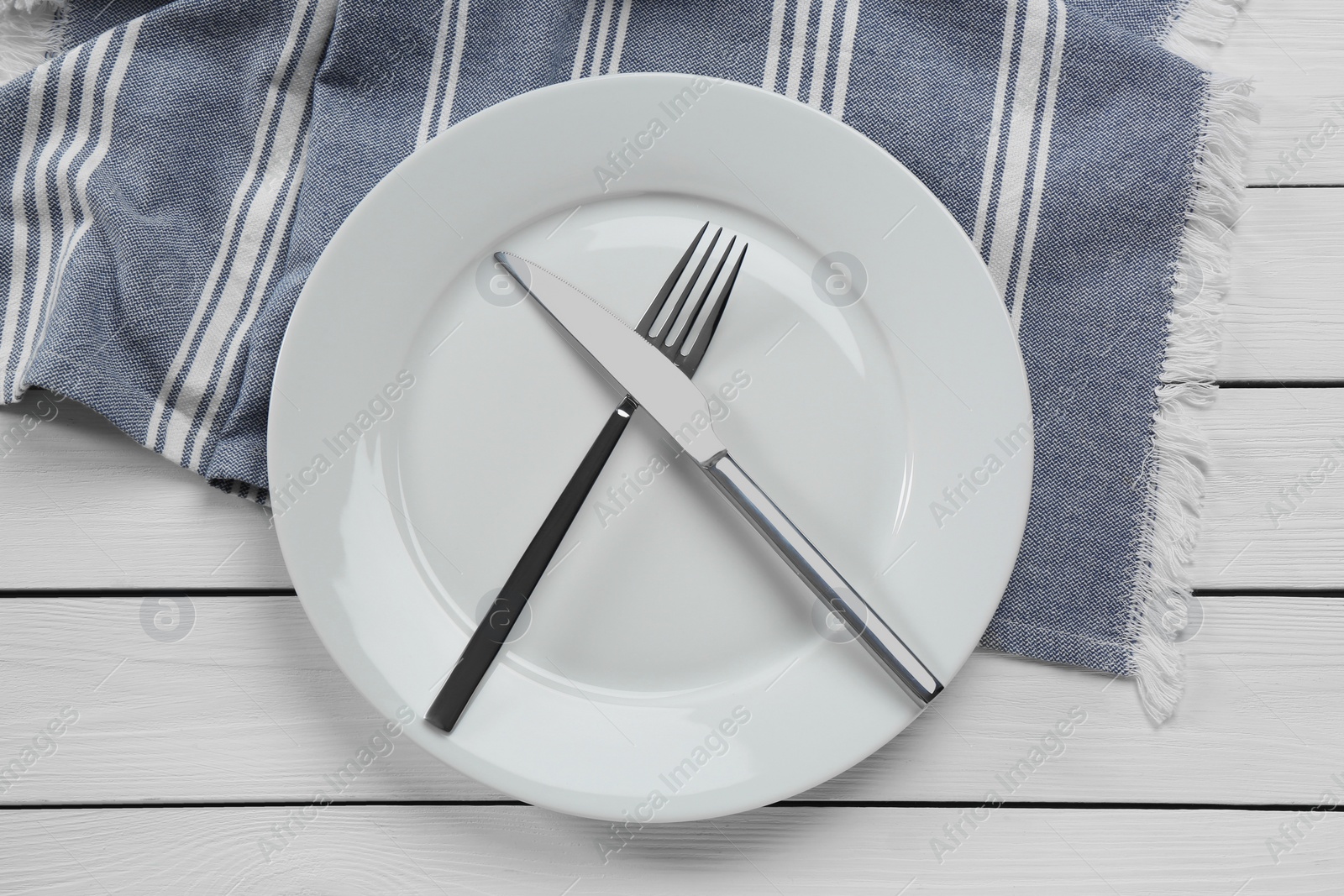 Photo of Clean plate with shiny silver cutlery on white wooden table, flat lay