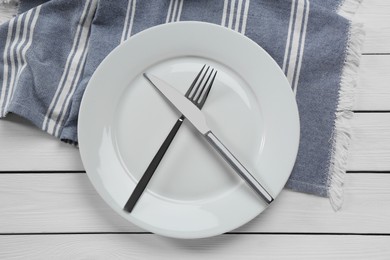 Clean plate with shiny silver cutlery on white wooden table, flat lay