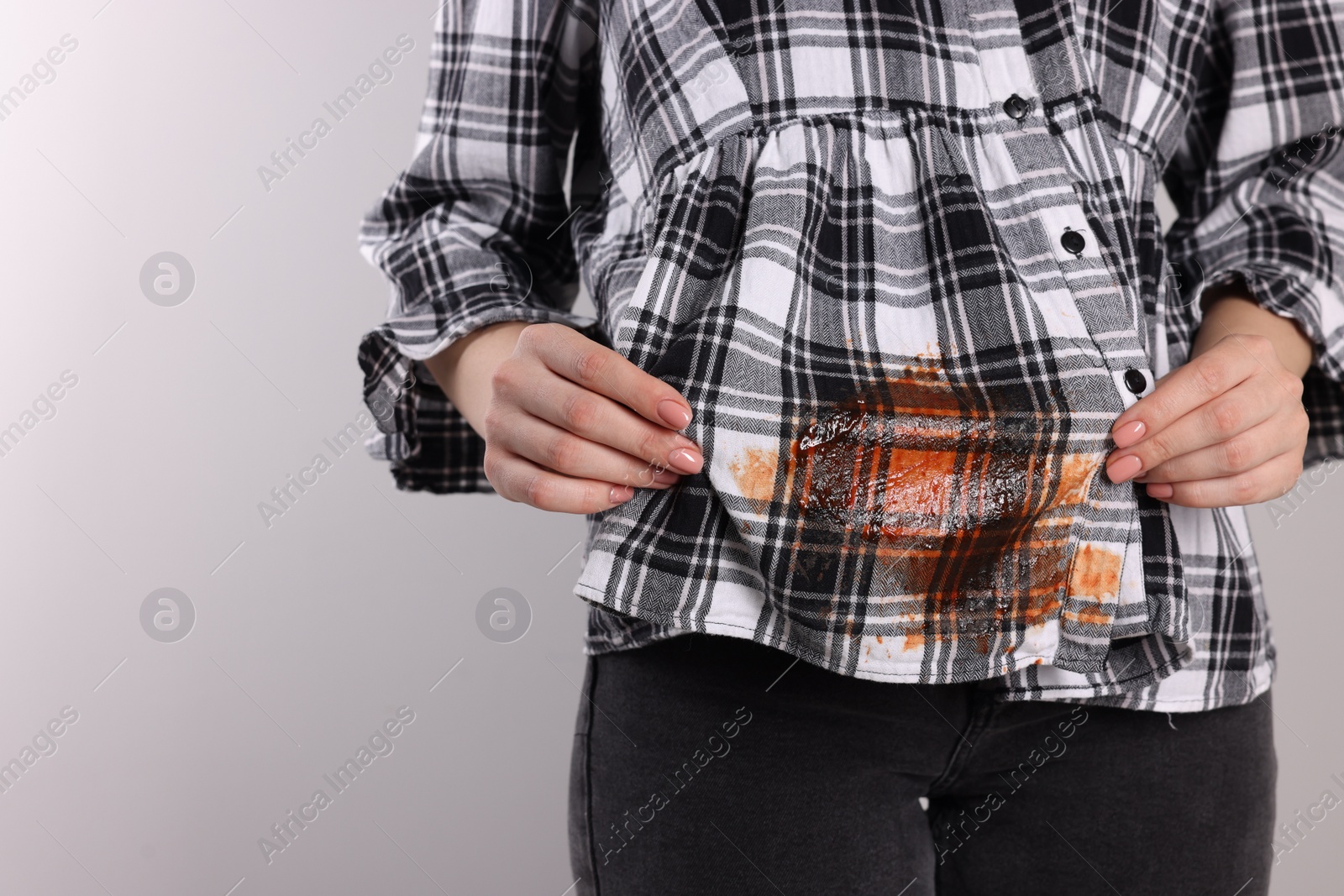 Photo of Woman showing stain from sauce on her shirt against light grey background, closeup. Space for text