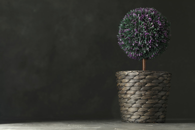 Artificial plant in wicker flower pot on grey stone table. Space for text