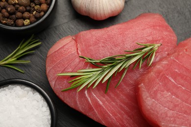 Fresh raw tuna fillets with rosemary and spices on black table, flat lay