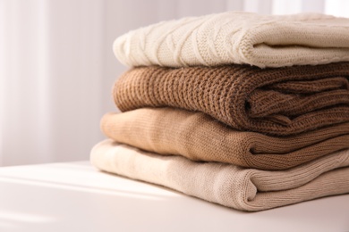 Stack of folded warm sweaters on white table indoors, closeup