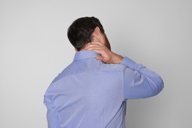 Man suffering from pain in his neck on light background, back view. Arthritis symptoms