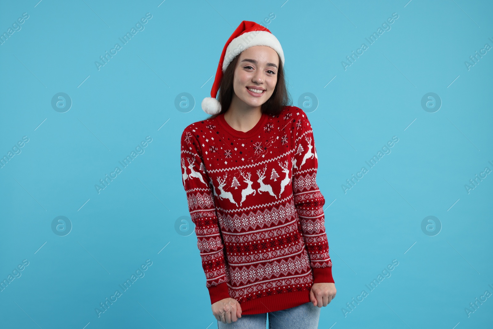 Photo of Happy young woman in Santa hat showing Christmas sweater on light blue background