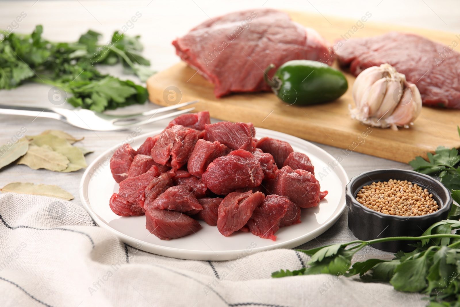 Photo of Plate with pieces of raw beef meat, spices and products on table