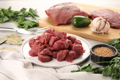 Photo of Plate with pieces of raw beef meat, spices and products on table