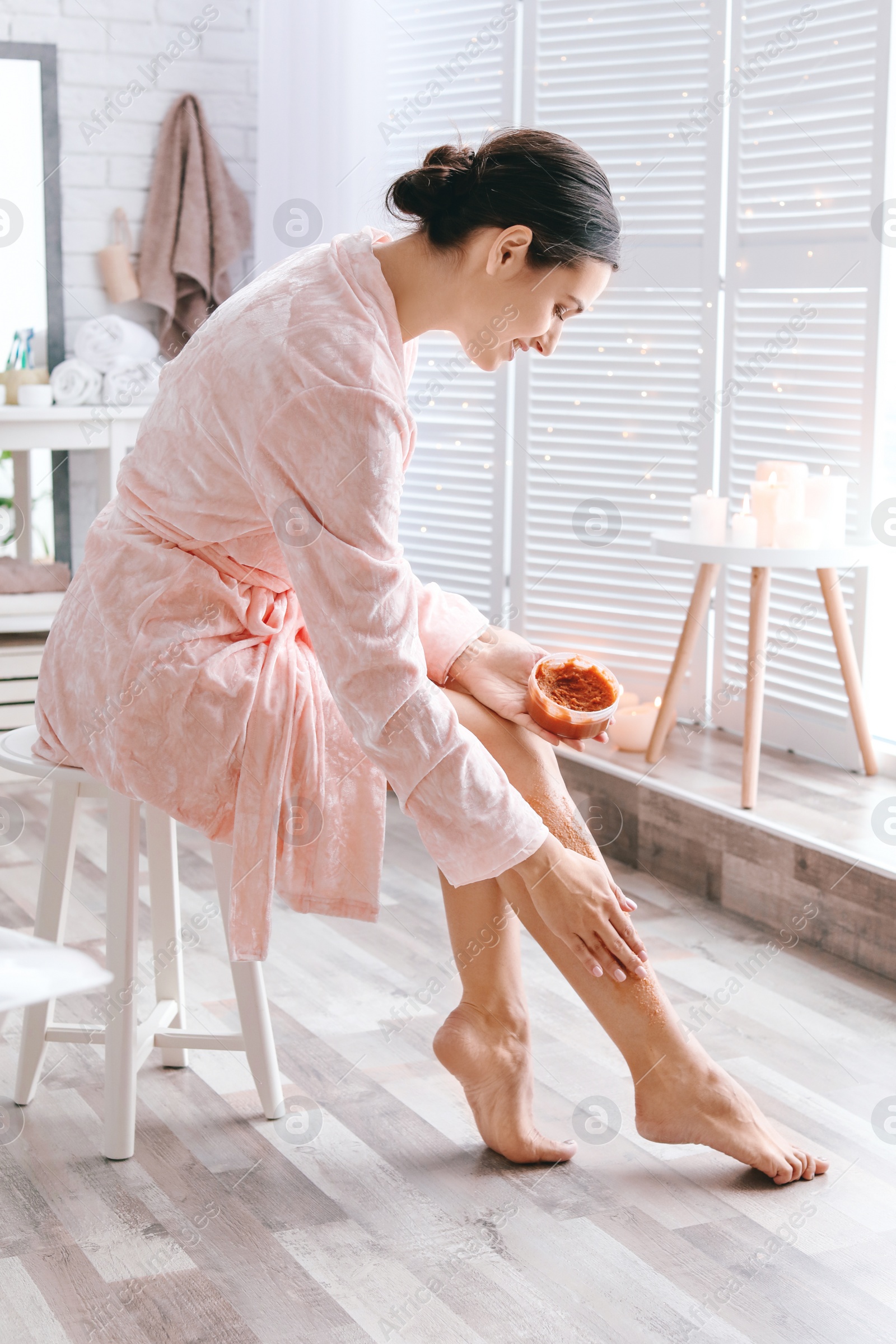 Photo of Young woman applying natural scrub onto her skin in bathroom