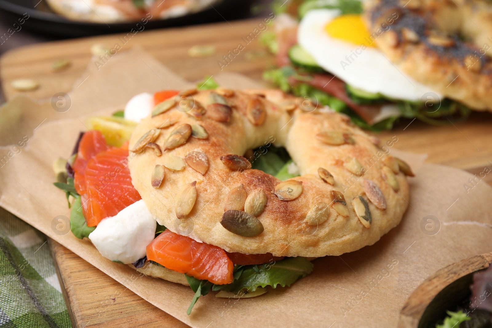 Photo of Tasty bagel with salmon, mozzarella cheese, tomatoes and lettuce on wooden board, closeup