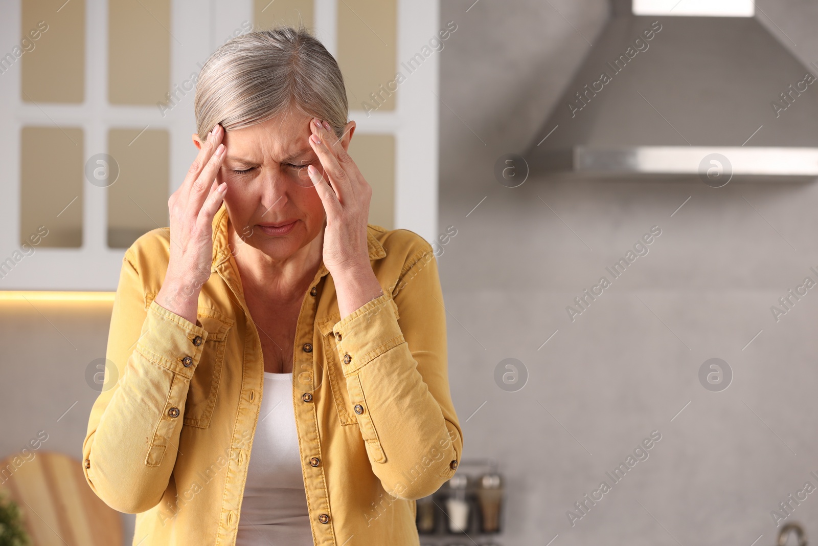 Photo of Menopause. Woman suffering from headache in kitchen, space for text