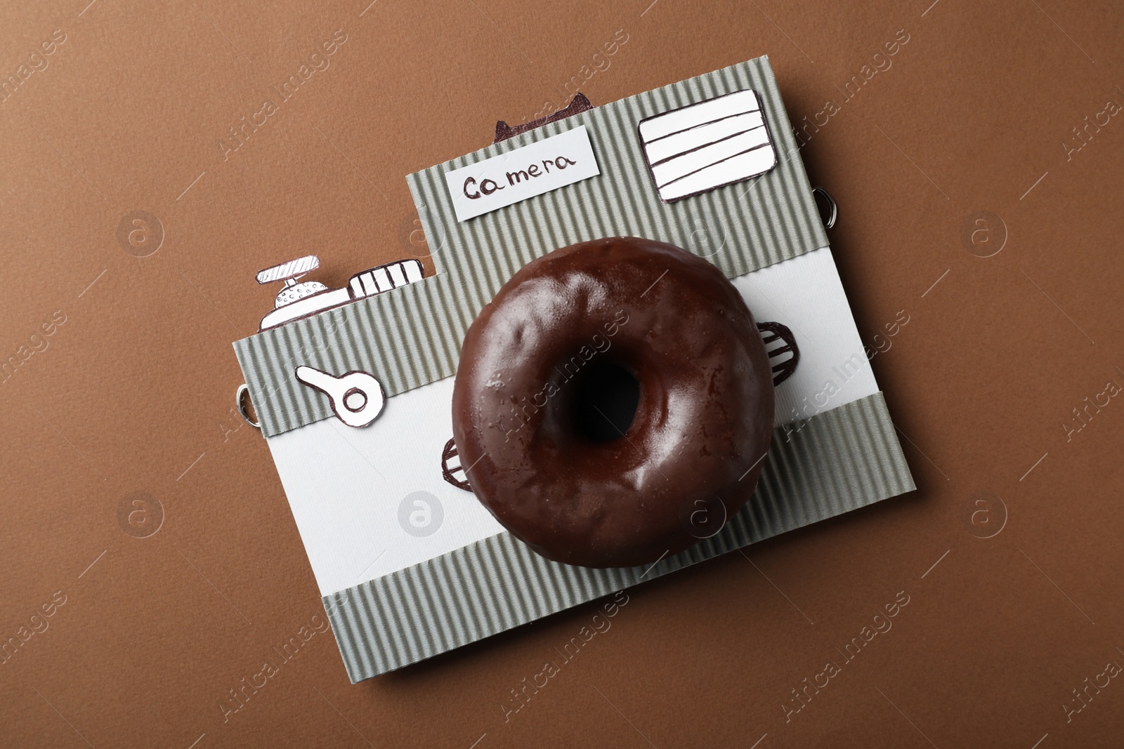 Photo of Camera made from donut and piece of cardboard on brown background, top view