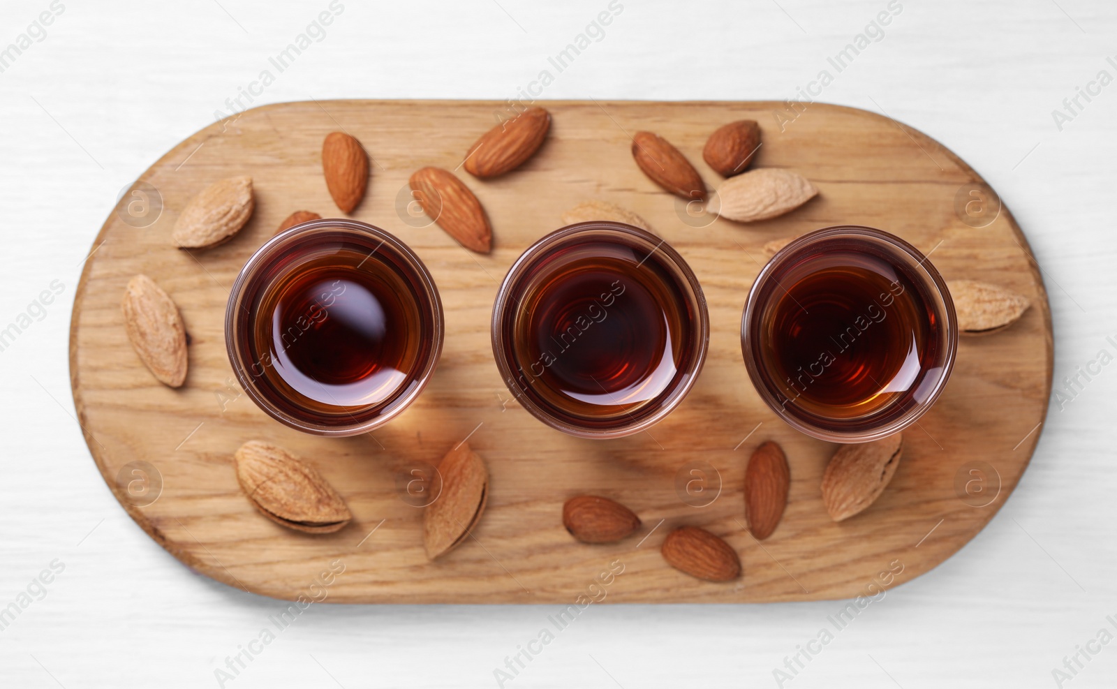 Photo of Shot glasses with tasty amaretto liqueur and almonds on white wooden table, top view