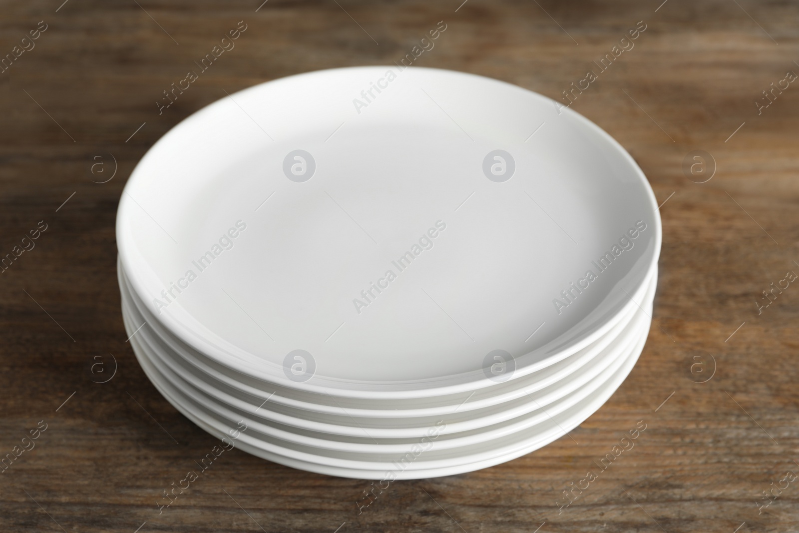 Photo of Stack of empty ceramic plates on wooden table, closeup