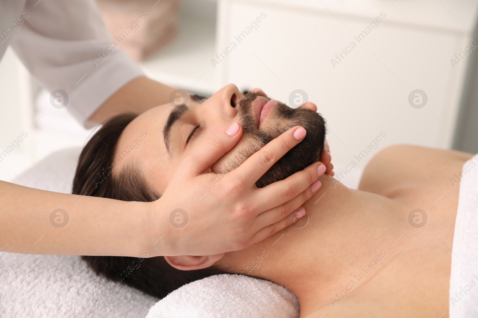 Photo of Young man receiving facial massage in beauty salon