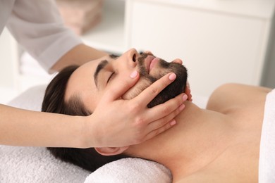 Young man receiving facial massage in beauty salon