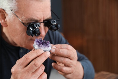 Photo of Male jeweler evaluating semi precious gemstone in workshop. Space for text