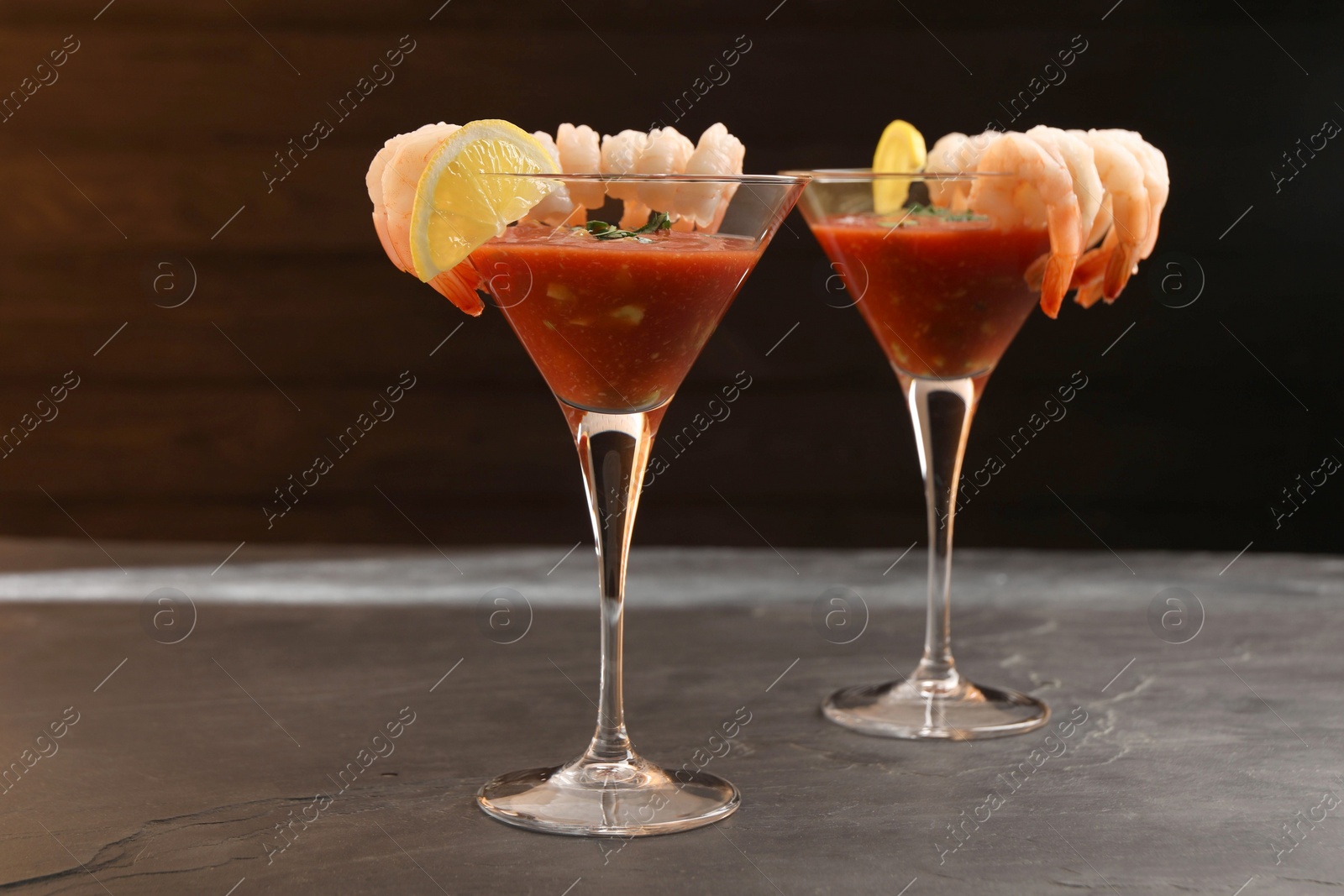 Photo of Tasty shrimp cocktail with sauce in glasses and lemon on grey textured table