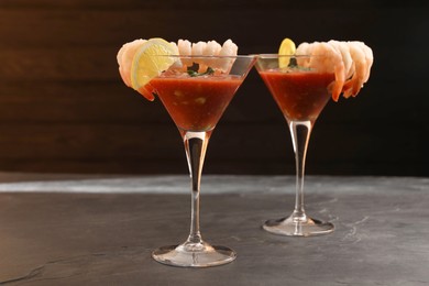 Tasty shrimp cocktail with sauce in glasses and lemon on grey textured table