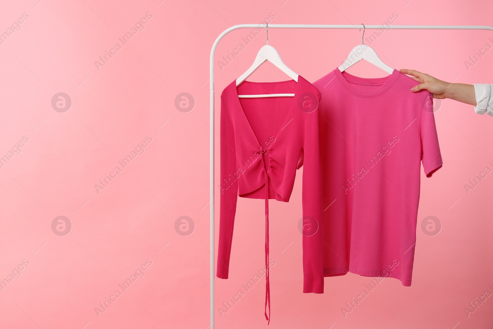 Photo of Woman taking stylish t-shirt from rack on pink background, closeup. Space for text