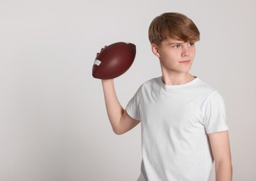 Teenage boy with american football ball on light grey background. Space for text