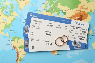 Photo of Honeymoon concept. Plane tickets and golden rings on world map, top view