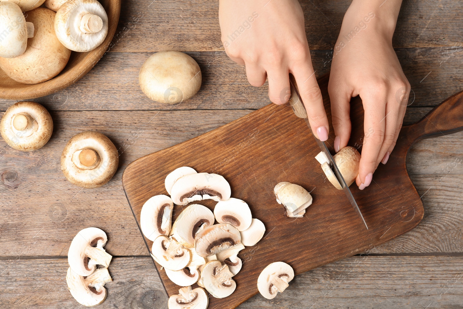 Photo of Young woman cutting fresh champignon mushrooms on wooden board, top view