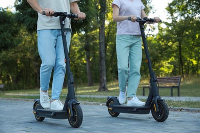 Photo of Couple riding modern electric kick scooters in park, closeup