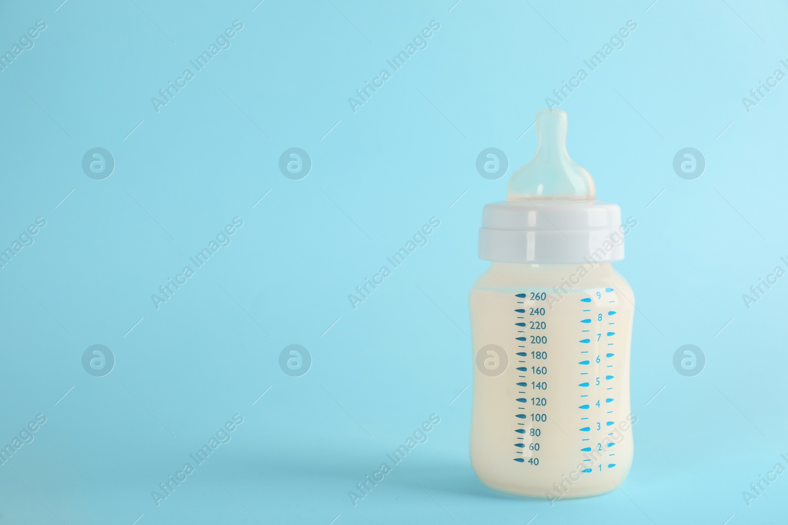 Photo of Feeding bottle with infant formula on light blue background, space for text. Baby milk