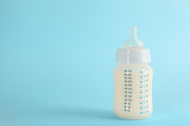 Photo of Feeding bottle with infant formula on light blue background, space for text. Baby milk