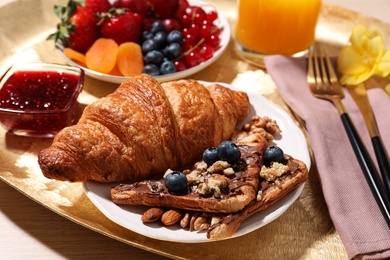 Delicious breakfast with croissant and fruits on wooden table, closeup
