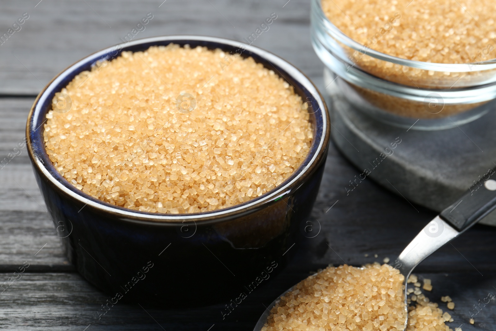 Photo of Brown sugar in bowls and spoon on black wooden table, closeup