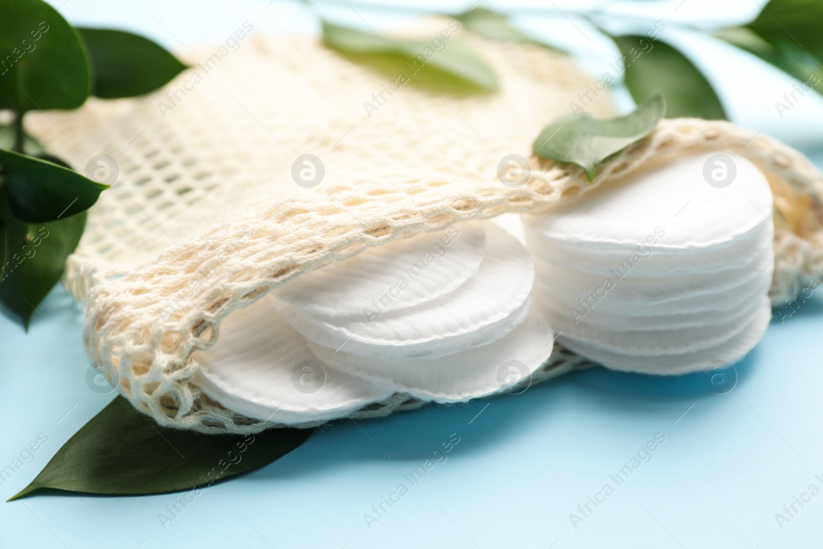 Photo of Cotton pads in bag and leaves on light blue background, closeup. Makeup removal equipment