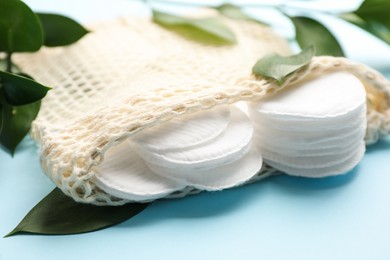 Photo of Cotton pads in bag and leaves on light blue background, closeup. Makeup removal equipment