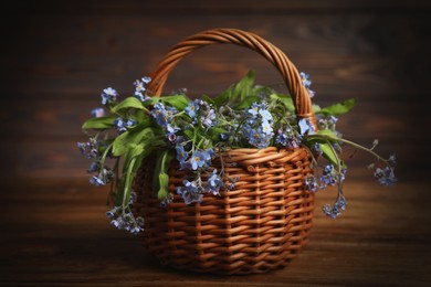 Photo of Beautiful forget-me-not flowers in wicker basket on wooden table