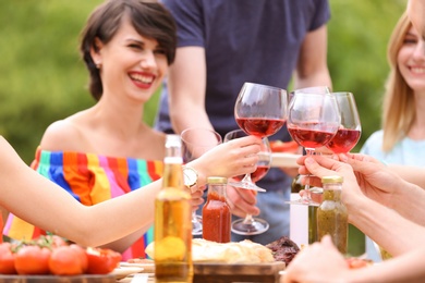 Photo of Young people with glasses wine at table outdoors. Summer barbecue