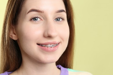 Photo of Portrait of smiling woman with dental braces on light green background, closeup. Space for text