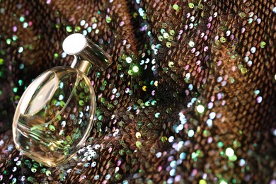 Photo of Luxury perfume in bottle on fabric with colorful sequins