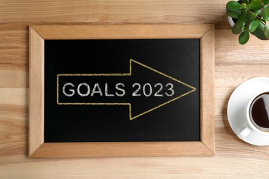 Image of Blackboard with drawn arrow and word GOALS on wooden background, flat lay